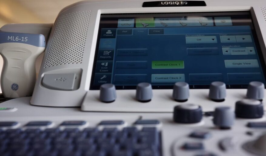 Close-up of a medical ultrasound machine control panel with knobs and a screen.