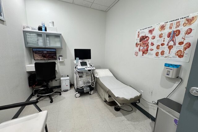 A clean medical examination room with a patient bed and medical equipment.